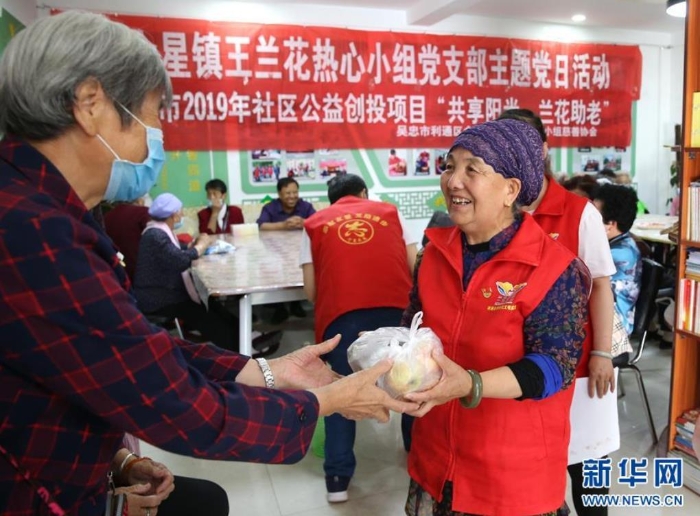 王兰花（右）向来到兰花志愿服务站参加活动的老人发放“爱心水果”（6月23日摄）。新华社记者 贾浩成 摄
