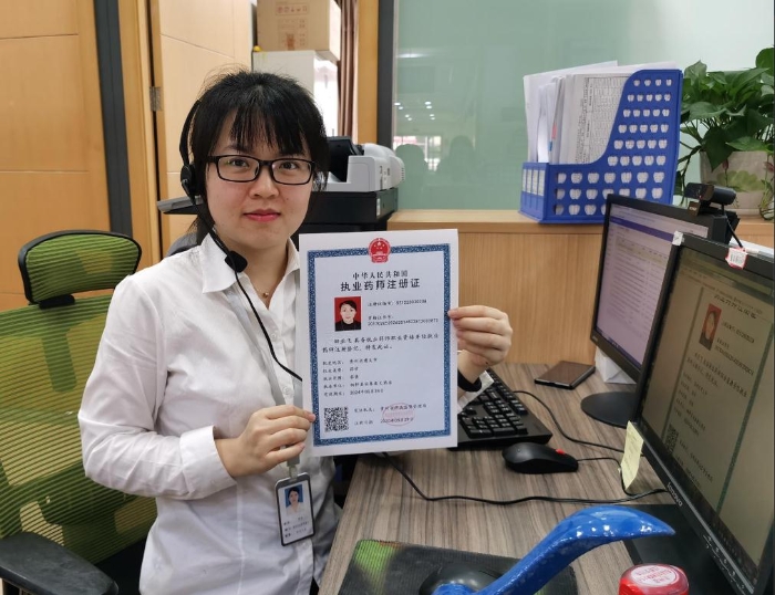 贵州省药品监管局窗口工作人员展示贵州首张异地办理的执业药师注册证