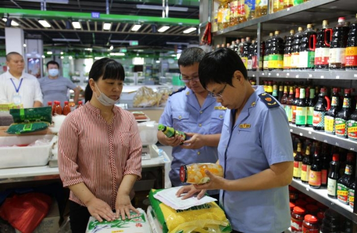 图为执法人员检查农贸市场内商超在售食品。