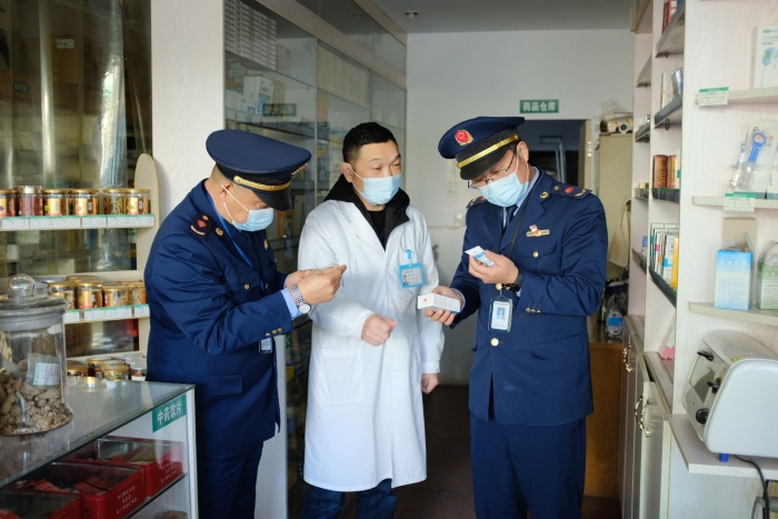 图为执法人员在一家药店检查其经销的药品外包装上标签是否规范，并核对相关购销登记台账的信息是否合规。